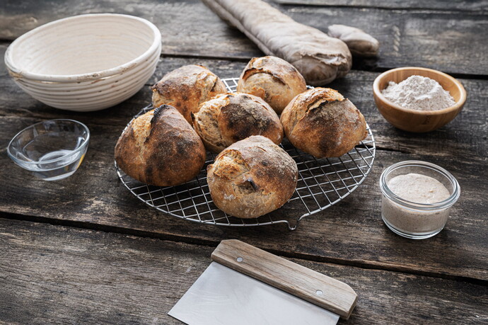 Frisch gebackene Sauerteigbrötchen auf einem Gitter mit Zutaten und Teig auf Holztisch