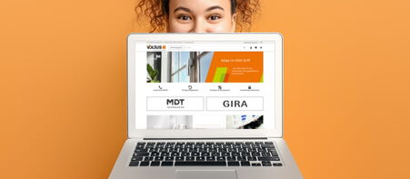 Frau hinter Laptop mit geöffneter Website auf orangefarbenem Hintergrund