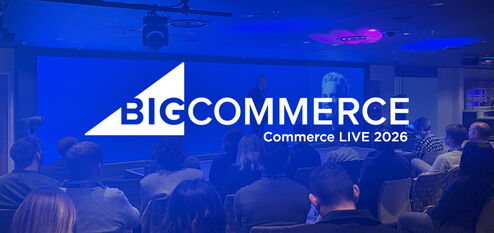 Publikum sitzt in einem Konferenzraum vor Bühne mit großem BigCommerce-Logo und Präsentation.