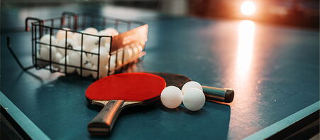 Tischtennisschläger mit Bällen und Korb auf blauer Platte in Halle