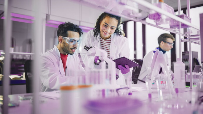 Forschende im modernen Labor arbeiten mit Mikroskop und Tablet unter violettem Licht