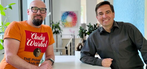 Ronny Büchner und Tino Favetto sitzen nebeneinander und lächeln in die Kamera.