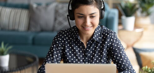 Frau sitzt vor einem Laptop mit einem Headset auf dem Kopf