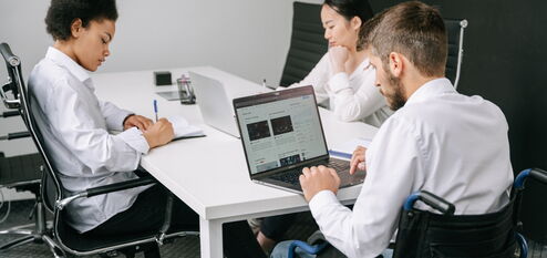 Drei Personen sitzen an einem Tisch und Arbeiten