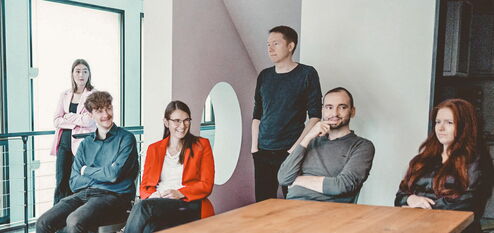 Sechs Mitarbeitende haben ein Meeting an einem Tisch und lächeln freundlich