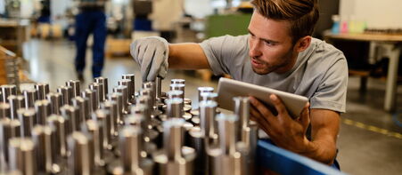 Mitarbeiter prüft Metallbauteile in der Produktion mit Tablet